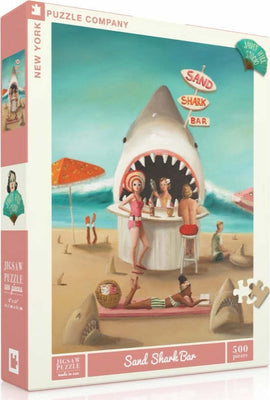 The packaging of the Sand Shark Bar jigsaw puzzle by New York Puzzle Company features a vibrant beach scene where people enjoy drinks at a bar shaped like a shark's mouth. The artwork showcases colorful umbrellas and beachgoers, inviting a fun summer atmosphere. The puzzle consists of 500 pieces and is perfect for puzzle enthusiasts of all ages.