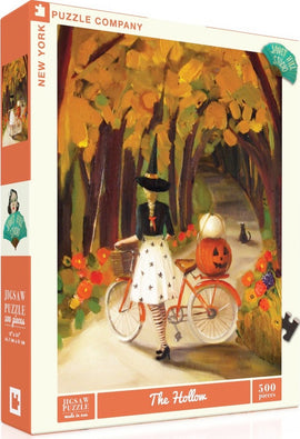 The Hollow jigsaw puzzle by New York Puzzle Company features a whimsical autumn scene with a woman in a witch costume riding a bicycle decorated with a pumpkin. The vibrant colors of the fall foliage blend beautifully with the intricate details of the woman's attire and the cheerful flowers surrounding her, creating a charming atmosphere perfect for seasonal enjoyment. This 500-piece puzzle is ideal for puzzle enthusiasts of all ages.