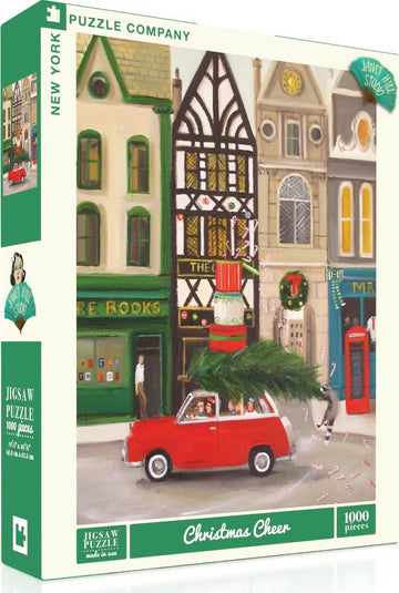 A colorful jigsaw puzzle titled 'Christmas Cheer' by New York Puzzle Company, depicting a festive scene with a red car carrying a Christmas tree, surrounded by charming shops and holiday decorations. The puzzle includes 1000 pieces and features whimsical artwork that captures the spirit of the season.