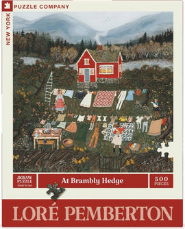 A colorful jigsaw puzzle titled 'At Brambly Hedge' by New York Puzzle Company. The image features a whimsical countryside scene with a red house, lush greenery, people hanging laundry, and a picturesque mountain backdrop. The puzzle consists of 500 pieces and showcases the charming artwork of Loré Pemberton.