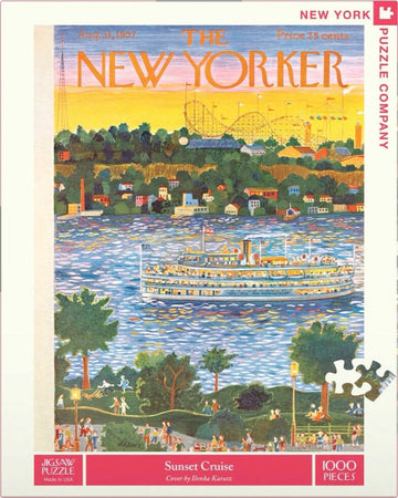 A colorful jigsaw puzzle featuring a scenic sunset cruise scene. The artwork, by Ilonka Karasz, illustrates a vibrant sunset over a body of water with a large steamboat, trees, and people enjoying a park. The sky blends hues of orange, pink, and blue, creating a warm and inviting atmosphere.