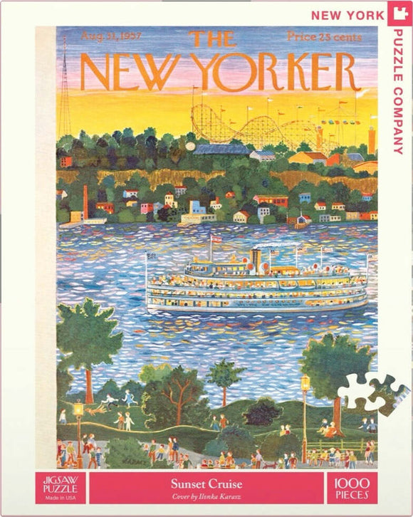 A colorful jigsaw puzzle featuring a scenic sunset cruise scene. The artwork, by Ilonka Karasz, illustrates a vibrant sunset over a body of water with a large steamboat, trees, and people enjoying a park. The sky blends hues of orange, pink, and blue, creating a warm and inviting atmosphere.