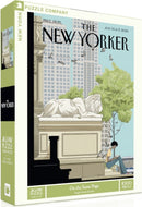 On The Same Page jigsaw puzzle by New York Puzzle Company featuring an illustration from The New Yorker. The box shows a tranquil urban scene with a person sitting beside a lion statue in a green park, surrounded by buildings and birds. The puzzle contains 1000 pieces, making it perfect for puzzle enthusiasts.