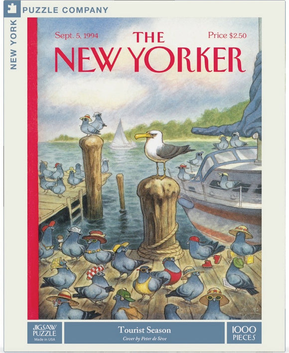A colorful jigsaw puzzle box titled 'Tourist Season' featuring a whimsical illustration by Peter de Seve. The scene depicts a group of cheerful bluebirds wearing various hats, standing on a wooden dock by the water, with a boat in the background. This 1000-piece puzzle showcases a playful and vibrant interpretation of nature.