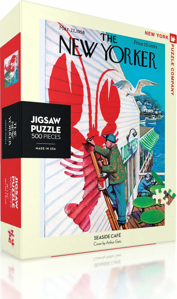 Seaside Cafe jigsaw puzzle by New York Puzzle Company featuring 500 pieces. The box displays a vibrant cover illustration by Arthur Getz, showcasing a picturesque seaside setting with a lobster motif and people engaged in leisurely activities. Perfect for puzzle enthusiasts and art lovers alike.