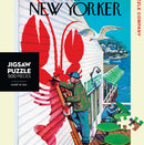 Seaside Cafe jigsaw puzzle featuring a vibrant illustration of a painter adding a large lobster mural to a seaside cafe. The scene captures the essence of coastal life with boats in the water and a serene atmosphere. Made in the USA, this 500-piece puzzle by New York Puzzle Company offers both a challenge and a charming artistic experience.