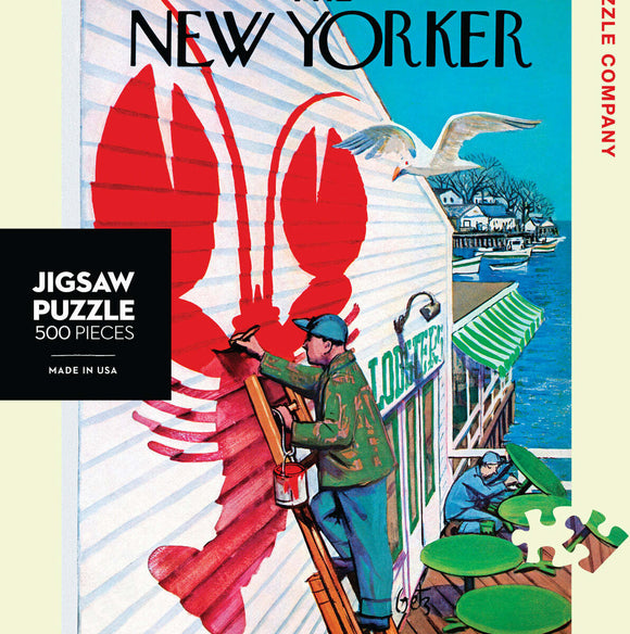 Seaside Cafe jigsaw puzzle featuring a vibrant illustration of a painter adding a large lobster mural to a seaside cafe. The scene captures the essence of coastal life with boats in the water and a serene atmosphere. Made in the USA, this 500-piece puzzle by New York Puzzle Company offers both a challenge and a charming artistic experience.