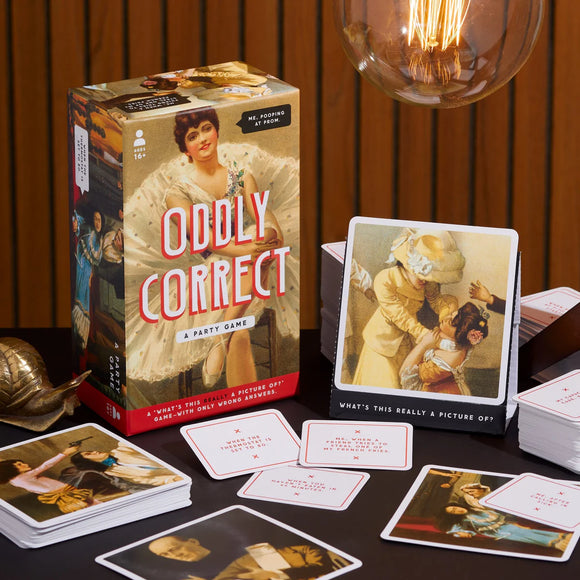Board game packaging and cards titled 'Oddly Correct' on a table with a warm background.
