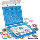 The Original Spirograph Deluxe Set by Kahootz displayed in an opened blue carrying case. The kit includes colorful circular templates, a drawing board, a red pen, various gears, and several completed spirograph designs in vibrant colors spread around.