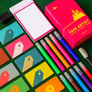 A Fake Artist Goes to New York Box and Components Laid Out Nearby; Colorful stationery items including markers and notepads on a green surface
