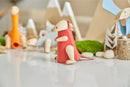 A DIY kit featuring a colorful wooden Tyrannosaurus figure by Plan Toys, displayed among other playful wooden animals and natural elements like moss and stones, perfect for creative play and learning.