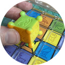 A close-up view of Tut's Tablet by Project Genius, showcasing a colorful mechanical puzzle. A hand holds a green and yellow block with hieroglyphics, positioned above a multi-colored grid with various symbols, including animals and Egyptian motifs. The intricate design emphasizes a combination of play and cognitive challenge, appealing to puzzle enthusiasts.
