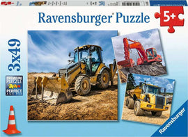 Ravensburger Diggers at Work jigsaw puzzle featuring three images of construction vehicles: a yellow backhoe loader, a red excavator, and a yellow dump truck, set against a blue sky. The puzzle is designed for ages 5 and up and is made with high-quality pieces for an ideal fit.