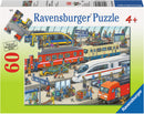 Ravensburger Railway Station jigsaw puzzle consisting of 60 pieces, featuring a busy train station scene with passengers, trains, and various activities happening around the platform. Suitable for ages 4 and up.