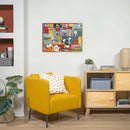 A colorful jigsaw puzzle titled 'Peanuts Moments' by Ravensburger. The puzzle features various characters and quotes from the Peanuts comic strip, displayed within a vibrant, patchwork background. The completed puzzle hangs on a light-colored wall above a cozy yellow armchair adorned with a patterned pillow. A wooden side table with decorative items complements the scene.