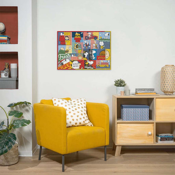 A colorful jigsaw puzzle titled 'Peanuts Moments' by Ravensburger. The puzzle features various characters and quotes from the Peanuts comic strip, displayed within a vibrant, patchwork background. The completed puzzle hangs on a light-colored wall above a cozy yellow armchair adorned with a patterned pillow. A wooden side table with decorative items complements the scene.