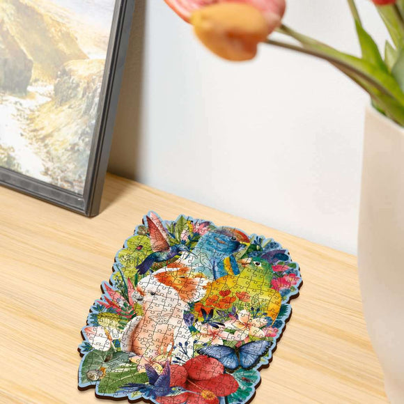 A completed 300-piece jigsaw puzzle titled 'Beautiful Birds' by Ravensburger, featuring vibrant birds and flowers. The puzzle is displayed on a wooden surface with a decorative vase in the background.