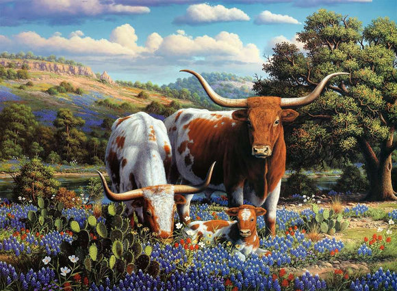 A beautifully illustrated 500-piece jigsaw puzzle featuring a serene scene of Longhorn cattle grazing among vibrant wildflowers in a picturesque landscape. The image showcases two adult Longhorns and a calf surrounded by lush greenery, colorful sunlit blooms, and gentle rolling hills under a blue sky with soft clouds.
