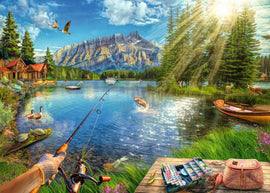 A scenic jigsaw puzzle featuring a beautiful lake landscape with fishing activities. The image showcases vibrant trees, mountains in the background, and wildlife including ducks and deer. A fishing rod and tackle box are in the foreground, adding to the lake life theme.