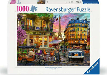 A 1000-piece Ravensburger jigsaw puzzle titled 'Paris at Dawn'. The image features a picturesque Parisian street scene with a boulangerie, blooming flowers, vintage cars, a bicycle, and the Eiffel Tower in the background against a beautiful sunrise sky.