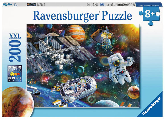 Ravensburger Puzzle featuring a cosmic exploration theme, depicting an astronaut floating in space among planets, stars, and the International Space Station. The box showcases a vibrant and colorful galaxy background filled with swirling cosmic elements, perfect for puzzle enthusiasts aged 8 and up.