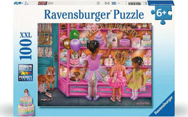The Ballet Bakery 100 pc Puzzle features a colorful illustration of three young girls in ballet tutus admiring an array of beautifully decorated cakes in a bakery. The display includes pink and purple cakes, colorful balloons, and a dog observing the scene, creating a delightful and enchanting atmosphere. Ideal for children aged 6 and above, this jigsaw puzzle is perfect for fostering creativity and fine motor skills.