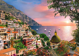 A vivid illustration of Positano, Italy, featuring colorful houses along the hillsides overlooking the sparkling blue sea. Sailboats dot the horizon under a stunning sunset sky with orange and pink hues. Lush greenery and blooming flowers enhance the scenic beauty, creating a serene and picturesque atmosphere, ideal for a Ravensburger jigsaw puzzle.
