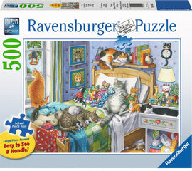 A 500-piece jigsaw puzzle titled 'Cat Nap' by Ravensburger, featuring a cozy bedroom scene filled with various cats lounging on a bed, with colorful decorations and a warm ambiance. The puzzle package showcases the artistic illustration, emphasizing the large piece format for easy handling.