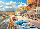 The Scenic Overlook 500 pc Large Format jigsaw puzzle by Ravensburger features a vibrant artwork depicting a picturesque viewpoint. The scene showcases a busy roadside with colorful retro cars, people dining under striped umbrellas, a scenic river, and a passing train amidst stunning mountainous landscapes. This nostalgic illustration captures a lively atmosphere, perfect for puzzle enthusiasts who appreciate detailed artistry and scenic views.