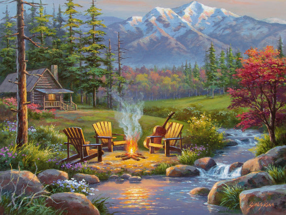 Ravensburger Riverside Livingroom 750-piece jigsaw puzzle featuring a tranquil landscape scene. The image showcases a cozy log cabin by a stream, surrounded by lush greenery, colorful flowers, and majestic mountains in the background. A warm campfire sits between wooden chairs, with a guitar resting on one of them, evoking a peaceful outdoor ambiance.