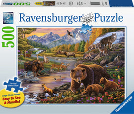 Wilderness 500 pc jigsaw puzzle by Ravensburger featuring a vibrant, detailed illustration of wildlife in a mountainous landscape. The scene includes a variety of animals such as moose, deer, bears, and wolves along a serene river, surrounded by lush trees and colorful flowers. The puzzle is designed in a large format with easily manageable pieces, ideal for both casual and experienced puzzlers.