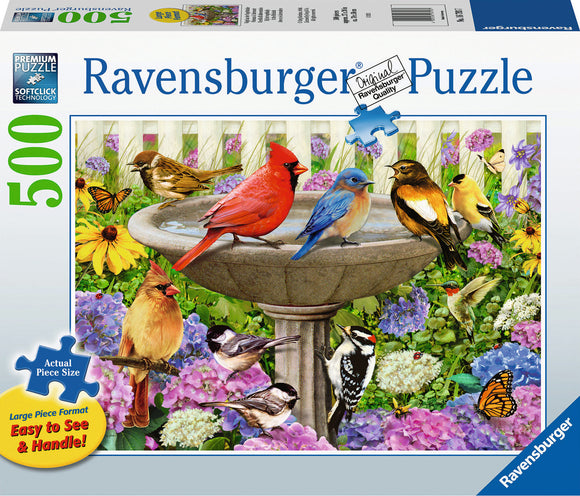 A colorful jigsaw puzzle box by Ravensburger featuring a vibrant scene of various birds, including a cardinal, bluebird, and others, gathered around a birdbath surrounded by flowers. The box highlights a '500' piece count and emphasizes the large piece format designed for easy handling.