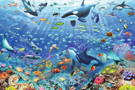 A vibrant jigsaw puzzle depicting a colorful underwater scene filled with various marine life including whales, dolphins, and colorful fish swimming among coral reefs. The artwork features intricate details of sea creatures like stingrays, jellyfish, and tropical fish in a bright blue ocean setting, evoking a lively underwater world.