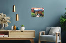 A beautifully illustrated jigsaw puzzle titled 'CreArt Beautiful Bavaria' by Creart. The artwork features a stunning landscape of mountains, a peaceful stream, and vibrant autumn foliage. The puzzle is displayed as wall art in a modern living room setting, with stylish decor elements like hanging lights, a wooden console, and decorative plants enhancing the aesthetic.