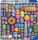 A colorful jigsaw puzzle featuring a vibrant array of painted beads in various patterns and designs. The puzzle includes 500 pieces and is produced by Ravensburger. The background showcases a lively mix of colors including bright pinks, blues, greens, and yellows.