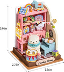 A detailed image of the DIY Childhood Toy House, a colorful miniature room set by Robotime. It features a pink shelving unit filled with playful items like books, colorful bags, and a cute bear figurine. The cozy setting includes a blue chair, a patterned floor, and decorative elements like a small clock and a drum. Sized at 3.94in height, 2.76in width, and 2.76in depth, this toy house captures a charming and whimsical atmosphere suitable for kids.