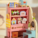 A beautifully crafted DIY Childhood Toy House by Robotime, showcasing a colorful wooden shelf filled with miniature items, including a yellow bag, a gumball machine, and a playful dog figure. The toy house radiates a nostalgic charm, featuring vibrant colors and intricate designs that inspire creative play.
