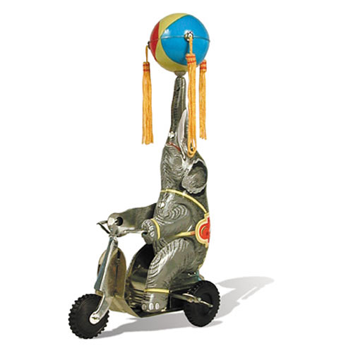 A colorful tin toy featuring an elephant riding a bike and balancing a beach ball on its trunk. The elephant is adorned with tassels and a decorative outfit, emphasizing a playful and whimsical design.