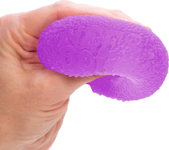 A hand holding a vibrant purple Needoh Gumdrop by Schylling. The textured surface is designed for sensory play and stress relief, showcasing the brand name 'Needoh' embossed on the product.