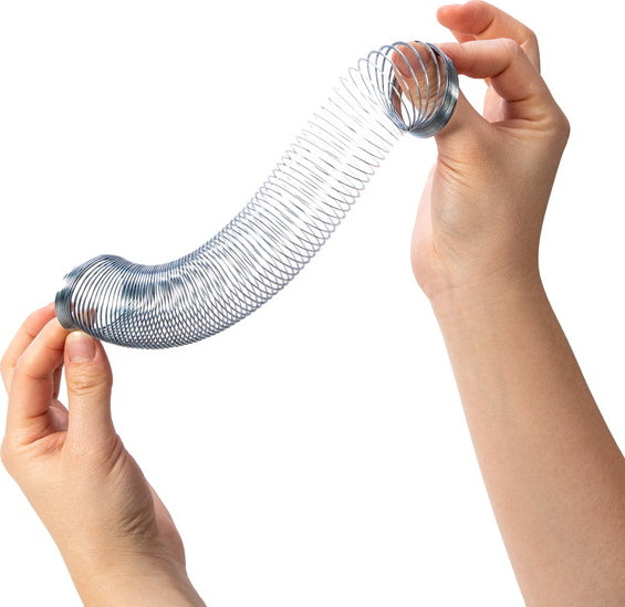 A person is holding a shiny metallic Mini Sproing toy, stretching it between their hands. The toy resembles a spring and is designed for playful engagement.