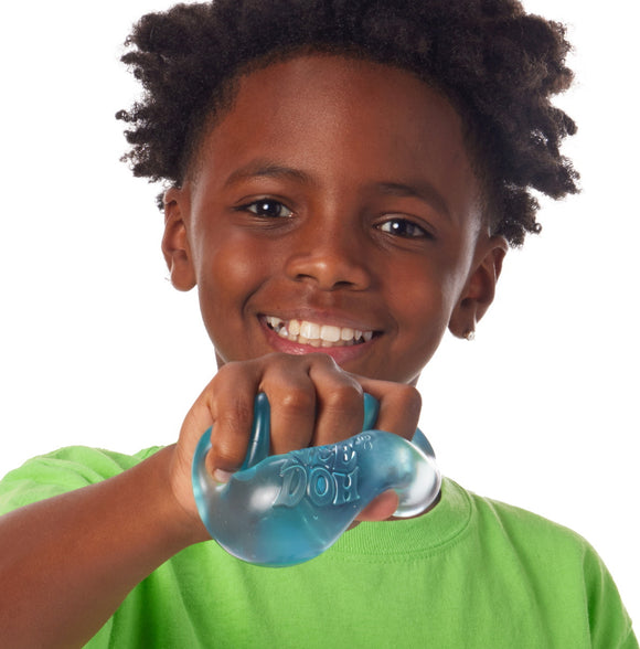 A joyful child with curly hair wearing a green shirt holds and squeezes the Nice Cube NEE DOH fidget toy, showcasing its blue, stress-relieving design.