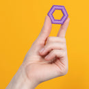 A hand holding a purple hexagonal piece made of small magnetic balls, set against a bright orange background. The hexagon showcases a unique geometric design, inviting tactile interaction.
