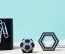 Speks Elements: Lunar features a colorful collection of magnetic balls, shaped into two distinct structures: a spherical form and a hexagonal shape. The objects are set against a soft blue background, with a sleek black container holding paper clips in the corner, creating a modern and minimalist workspace aesthetic.