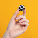 A hand holding a small, black and white spherical fidget toy resembling a soccer ball, set against a bright yellow background. The toy's intricate design features small beads that create a textured surface, making it visually appealing and satisfying to touch.