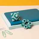 A colorful set of Speks Elements: Marine, featuring a decorative fidget toy in intricate designs made of teal and white magnetic beads. The items are displayed on a layered background of notebooks and paper clips, emphasizing their artistic and playful nature.