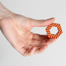 A person holds a hexagonal shape made of small magnetic balls in shades of orange and beige. The design is intricate, showcasing the versatile construction possibilities of the Speks Elements: Solar product.