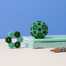 The Speks Elements: Terra is a playful collection of colorful magnetic beads, featured here with a star-shaped structure and a round formation. Set against a soft blue backdrop, they are placed on a mint-colored notebook accompanied by a stylish pencil, showcasing their vibrant greens and blues. Perfect for stress relief and creative exploration.