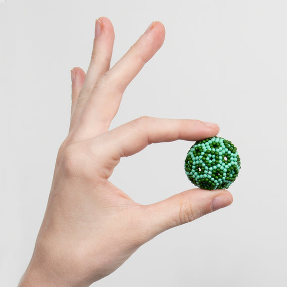 A hand holding a colorful sensory fidget toy, Speks Elements: Terra, featuring a textured surface with green and light blue beads that resemble a small globe.