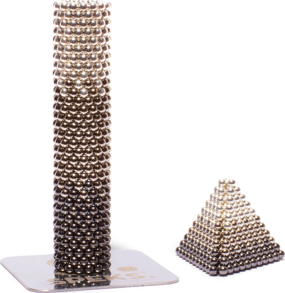 The Speks Reflect Gradient features a collection of shiny metal balls, designed for creative building. This set includes structures such as a tall cylindrical tower and a smaller pyramid shape formed from magnetic beads. Ideal for stress relief and enhancing focus, it combines fun and functionality.