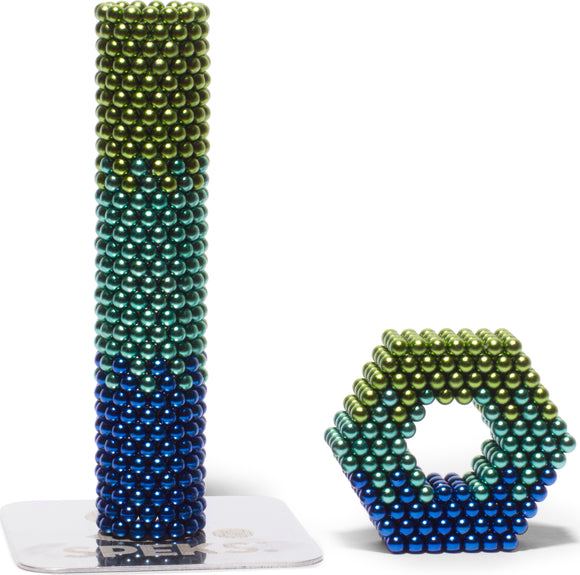 The Speks Soothe Gradient set features colorful magnetic spheres in a gradient of green and blue, forming a tall cylindrical tower and a hexagonal shape. This versatile toy encourages creativity, dexterity, and stress relief, making it perfect for both adults and children.